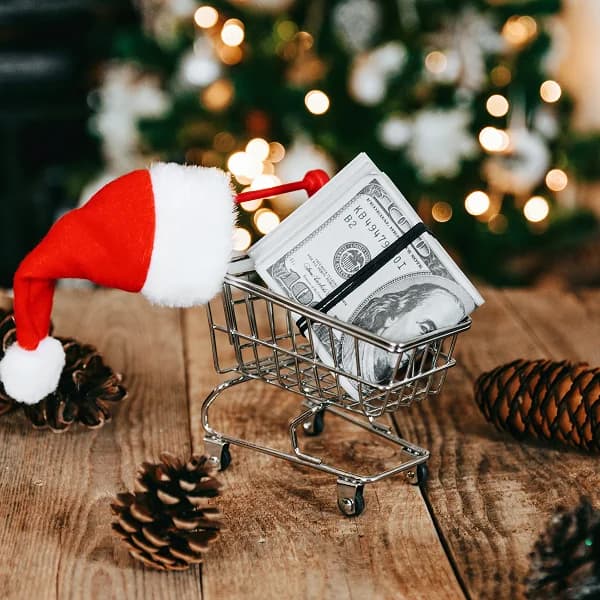 A mini shopping cart holding a stack of cash, beside a Santa hat and Christmas lights, illustrating holiday loans in Canada.