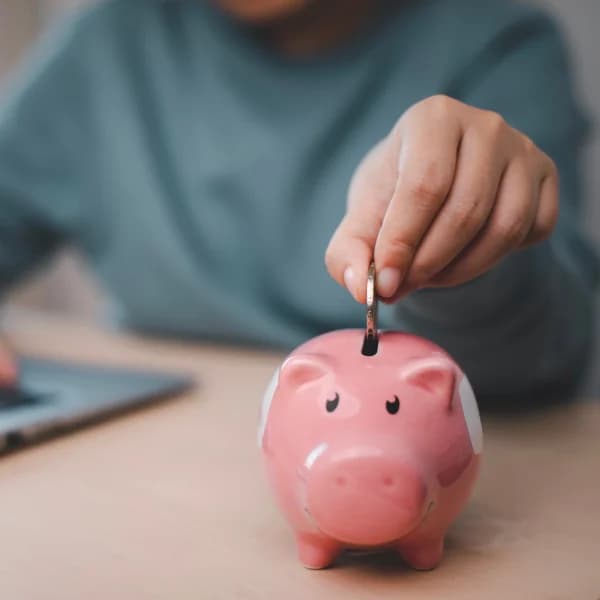 Une personne insérant de l'argent dans une tirelire, symbolisant l'épargne et la gestion des finances personnelles.