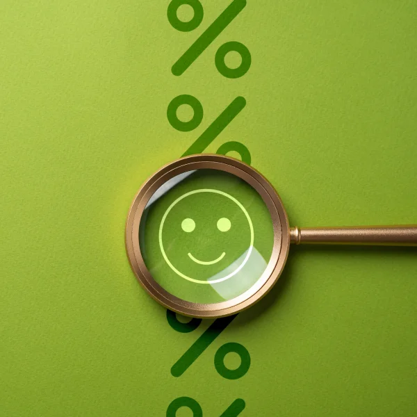 L'image montre une loupe avec un symbole de pourcentage et un visage souriant sur un fond vert, symbolisant une bonne cote de crédit.