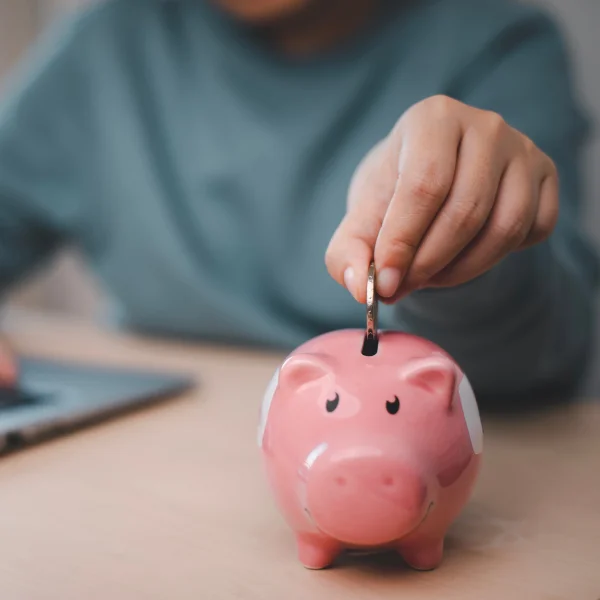 Une personne insérant de l'argent dans une tirelire, symbolisant l'épargne et la gestion des finances personnelles.