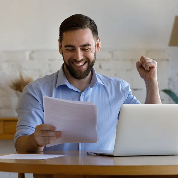 A man sitting at a table with a laptop and a document, preparing a financial file.