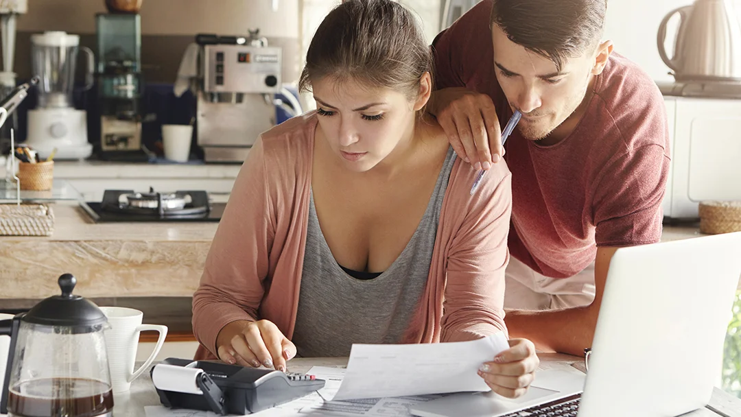 AA man and woman review paperwork on a laptop, focusing on a credit file together.