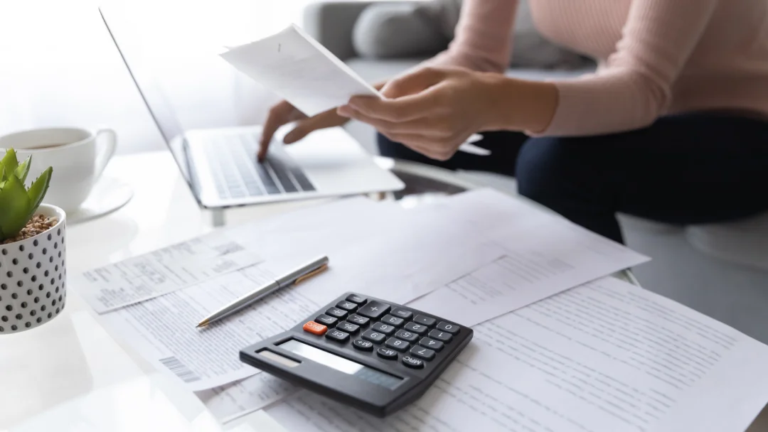 Woman working on a laptop with documents on the table, concentrating on her personal finances.