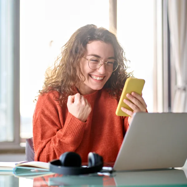 A woman smiles while using her phone and laptop, representing the convenience of Loans 24/7 services.
