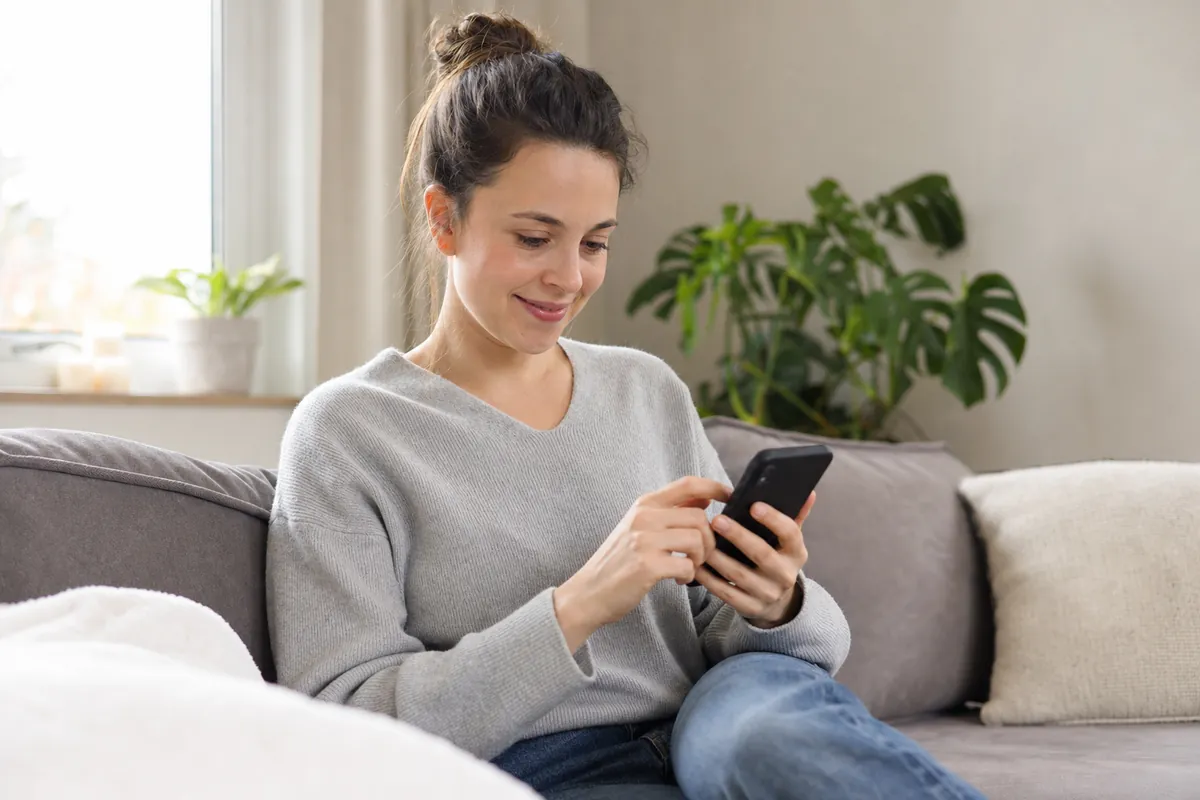 Une femme installée sur son divan fait une demande de petit prêt en ligne avec son téléphone
