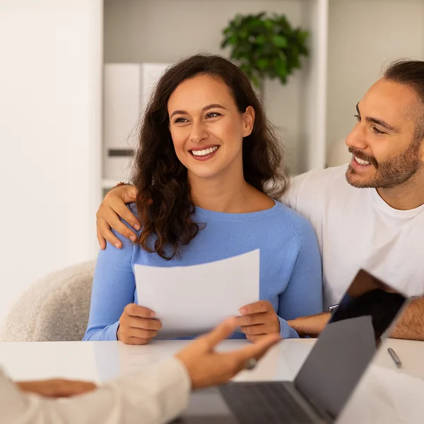 A man and woman sit at a table with a laptop and papers, discussing a small personal loan.