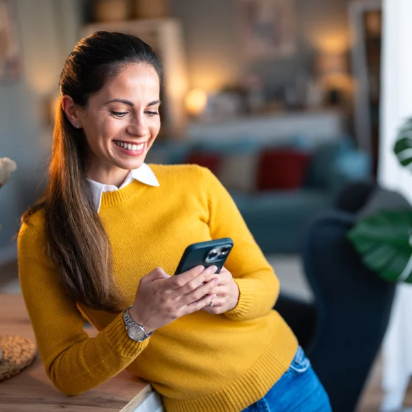 A woman in a yellow sweater smiles while using her phone, likely engaging with interac e-transfer services.
