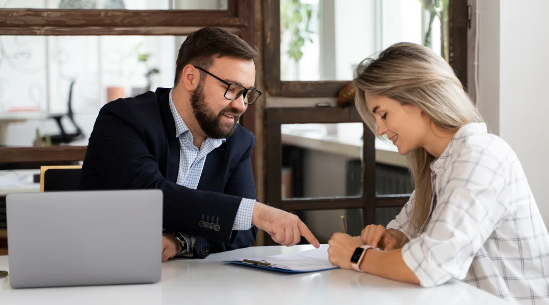 A man and woman sit at a table with a laptop, discussing options as independent lenders.