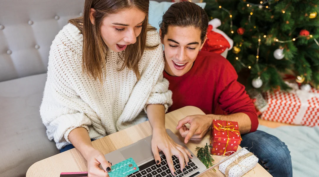 A woman holds cash in front of a laptop, symbolizing holiday loans and financial planning.nels.