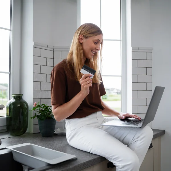 A woman sits on a kitchen counter with a laptop and credit card, exploring options for a same-day loan.