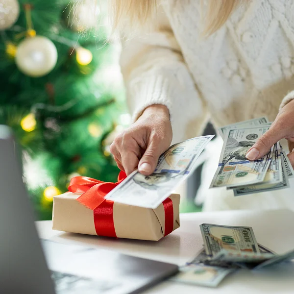 A woman holds cash in front of a laptop, symbolizing holiday loans and financial planning.